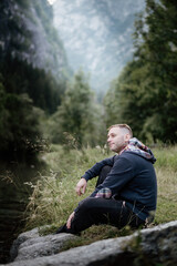 Forty-year-old man sitting on a rock in the mountains in the forest. Adventure during vacation. Outdoor activities and relaxation.