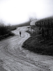 Cyclist with helmet on head cycling and sporting on mountain road in winter with morning fog, black and white.