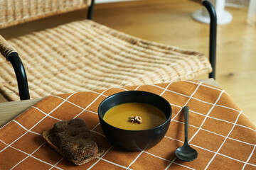 Fototapeta premium Pumpkin puree soup with walnuts with bread and a spoon on a brown checkered tablecloth against the background of a chair