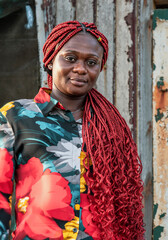 African woman with braided red dreadlocks hair and colorful shirt standing against a worn wall in Accra Ghana.