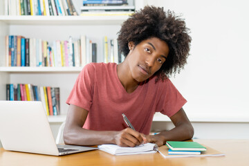 Smart black male student learning with books and computer