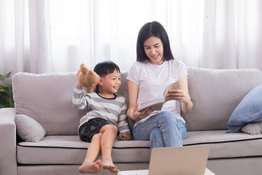 Asian beautiful mother and son read favorite book together on weekends, young woman and adorable boy lying down on sofa reading a comic book in living room, Enjoy listening to stories from mom.