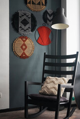 A rocking chair stands against the background of a gray wall with boho panels hanging on it