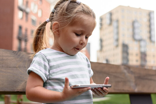A little cute girl sits on a bench and looks at a smartphone, phone addiction