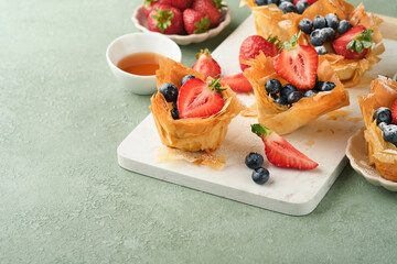 Phyllo or filo pies with fresh berries strawberries and blueberries, cheese filling topped with fresh mint on white plate. Homemade Filo pastry paskets. Delicious filo pastry dessert.