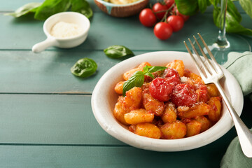 Potato gnocchi. Traditional homemade potato gnocchi with tomato sauce, basil and parmesan cheese on turquoise rustic kitchen table background. Traditional Italian food. Top view.