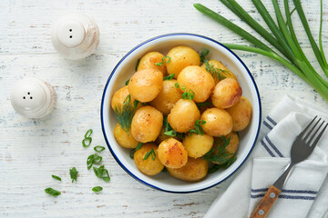 Boiled new or young potatoes with butter, fresh dill and onions in white bowl on white old rustic wooden background. Tasty new boiled potatoes. Top view.