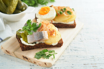 Open sandwich or smorrebrod with rye bread, herring, eggs, caramelized onions, parsley and cottage cheese on old wooden rustic table backgrounds. Danish or Scandinavian traditional food snack lunch.