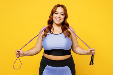 Young fun chubby overweight plus size big fat fit woman wear blue top warm up training look camera hold in hand skipping rope isolated on plain yellow background studio home gym Workout sport concept - obrazy, fototapety, plakaty