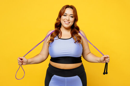 Young fun chubby overweight plus size big fat fit woman wear blue top warm up training look camera hold in hand skipping rope isolated on plain yellow background studio home gym Workout sport concept