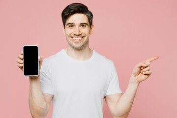 Young happy man wear white t-shirt casual clothes hold in hand using mobile cell phone in blue case with blank screen workspace area point aside isolated on plain pastel light pink background studio.