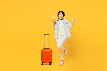 Traveler woman wear casual clothes denim shirt hold suitcase passport ticket isolated on plain yellow background. Tourist travel abroad in free spare time rest getaway Air flight trip journey concept