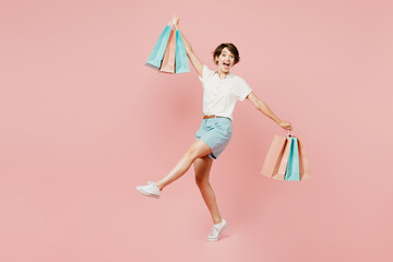 Full body young happy woman wear casual clothes hold shopping paper package bags stand on toes with...
