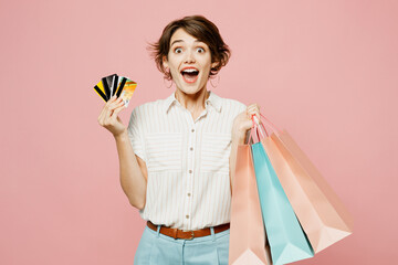 Young fun woman wear casual clothes hold shopping paper package bags, mock up of many credit bank card isolated on plain light pastel pink color background studio. Black Friday sale buy day concept.