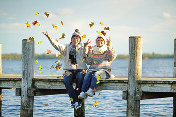 aktives Paar wirft buntes Laub hoch am See im Herbst