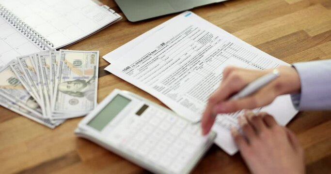 Woman is handwriting US 1040 tax form and using calculator. Individual tax return taxation and time to pay concept