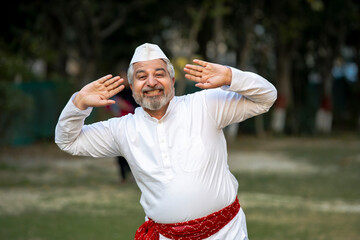 Happy indian senior man in traditional wear and dancing at garden