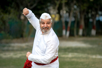Happy indian senior man in traditional wear and dancing at garden