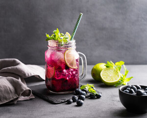 Refreshing blueberry mojito or lemonade with lime, mint and ice on a dark background. Summer healthy non-alcoholic drink made from fruits and berries. - obrazy, fototapety, plakaty