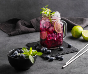 Refreshing blueberry mojito or lemonade with lime, mint and ice on a dark background with napkin...