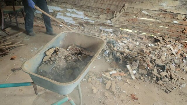 Collection of construction waste with a shovel in a wheelbarrow. Dismantling of a wooden house.