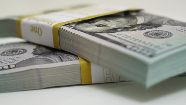 stack of bank bundles with US dollars on a white background. Close-up shot of new, freshly printed hundred-dollar bills rotating on a table. cash flow, business investment, or big money concepts.