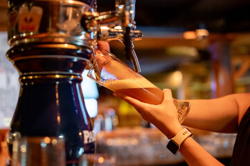 Fototapeta na wymiar bartender woman hand at beer tap pouring a draught beer in glass serving in a restaurant or pub