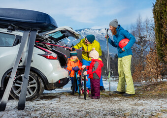Family mom dad and two children unload ski from car by mountain