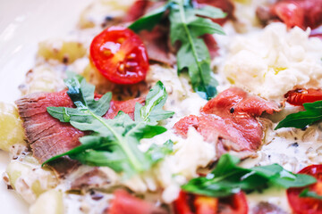 meat potato salad with tomatoes and pieces of beef on a plate in a cafe. light summer salad with potatoes and meat from a coffee house