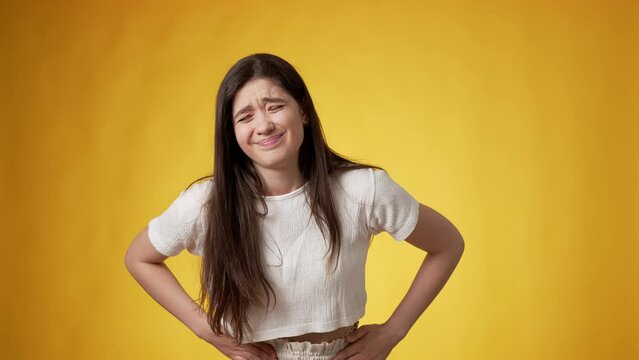 Distressfully looking casually dressed young woman with long dark hair touching her tummy with both hands apparently experiencing acute stomach pain against amber background