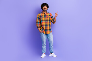 Full length photo of good mood man dressed plaid shirt denim pants indicating at product empty space isolated on purple color background