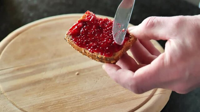 Toast with jam. hands spread jam on bread on the kitchen table.View from above. Whole grain bun with raspberry jam. 4k footage