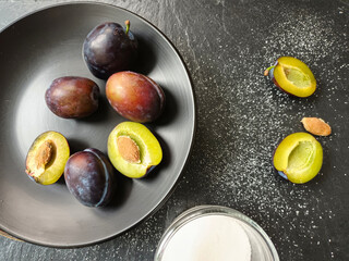 Zwetschgen auf einem schwarzen Teller und ein Glas Zucker