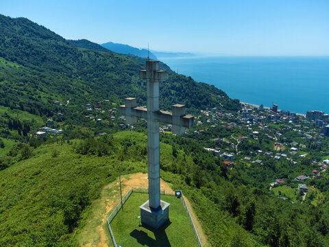 Close-up from the drone of the Orthodox cross on the mountain against the background of the sea, mountains and the village, Georgia. Concept of freedom, Christianity, Orthodoxy