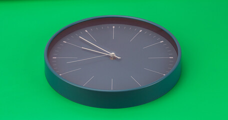 Black wall clock showing 9:52 AM. on a green background.
