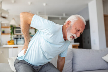 Senior man, with back pain, touches his back, illustrating sciatica and sedentary lifestyle....