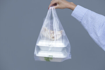 Woman's hands holding PVC plastic bag with takeaway foam lunch boxes. Single use food containers,...