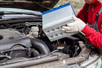 auto mechanic replaces the battery on the car. The man holds the battery and inserts it into the mounting compartment