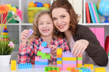 Cute little girl and her mother playing colorful plastic blocks