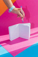 A school notebook on a bright multicolored background and a hand with a pen - 630643019