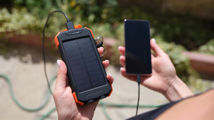 Hands holding a solar energy bank and mobile phone for recharging. Smartphone charging