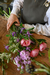 Faceless florist holding bunch of flowers on table