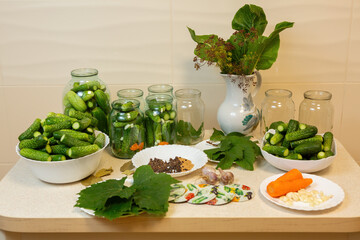 On the table are jars and plates of fresh cucumbers and other ingredients for canning