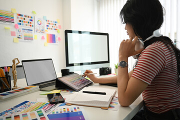 Young creative woman working with color palette, choosing color samples for design project at graphic studio.