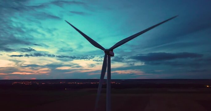 Aerial view wind turbines generate renewable energy at night. Silhouettes of windmills with bright lights on propellers rotate against dark sky