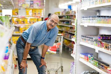 Indian senior citizen giving doing a shopping and giving expression at grocery shop.