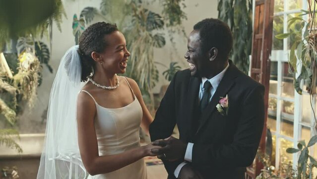 Medium shot of young well-dressed African American couple chatting while standing in beautiful place of their wedding ceremony filled with living green plants