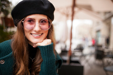 Stylish young attractive woman in beret and sunglasses sitting in cafe and looking away. Copy space.