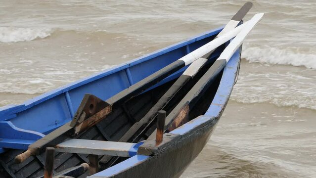 Bow of currach boat and traditional wooden oars piled onto front as waves crash
