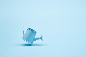 Bright blue garden watering can hover over the surface of the bright solid fond plain bright blue...